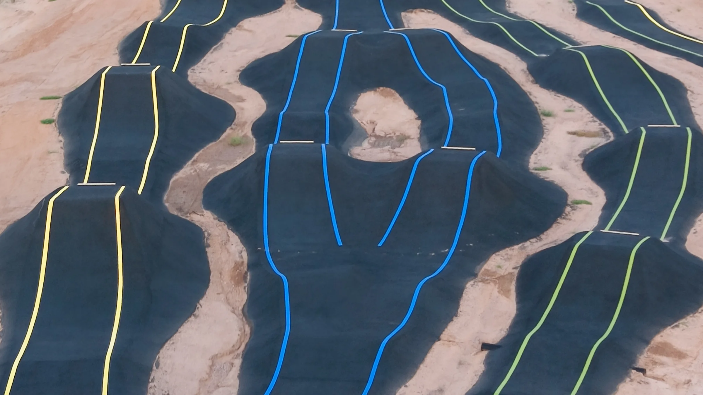 Close aerial view of rounded paved rollers and banked curves outlined with blue, yellow and green markings.