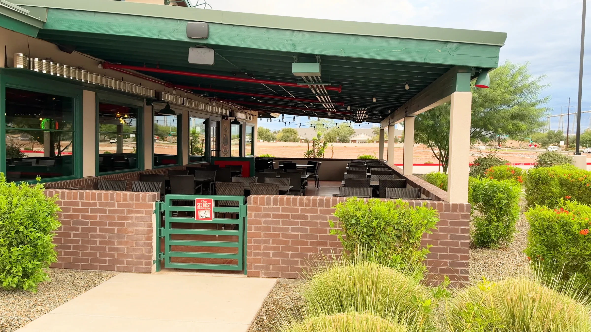 Covered Oregano’s patio with rows of tables and chairs, string lights, brick walls and a green entrance gate.