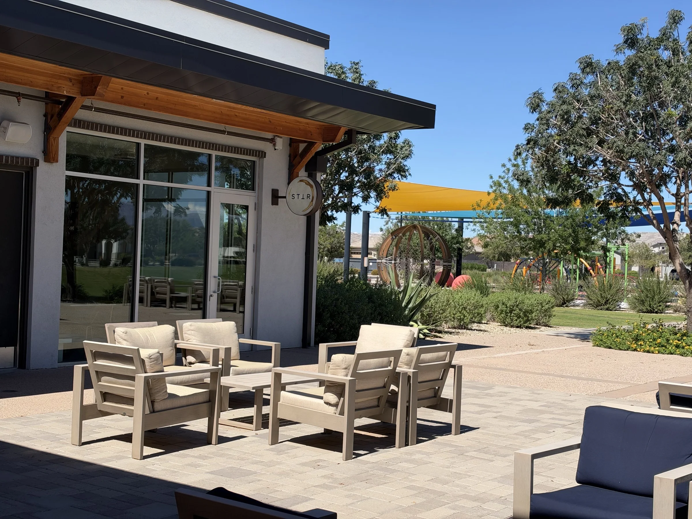Outdoor lounge seating beside STIR at Cadence at Gateway, with a shaded playground beyond the patio.