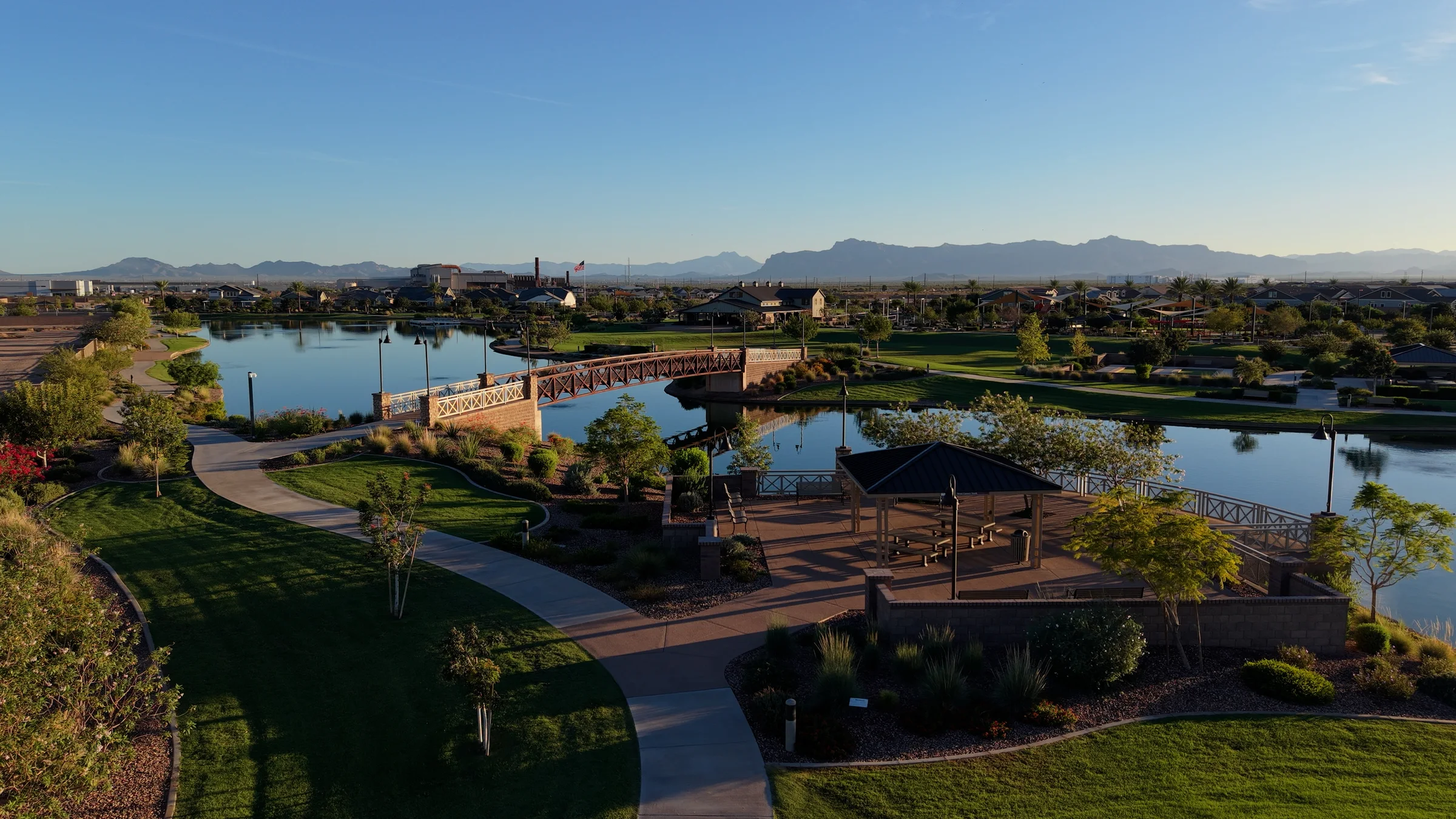 Aerial view of Barney Farms lake, pedestrian bridge, waterfront ramada and landscaped paths with mountains on the horizon.