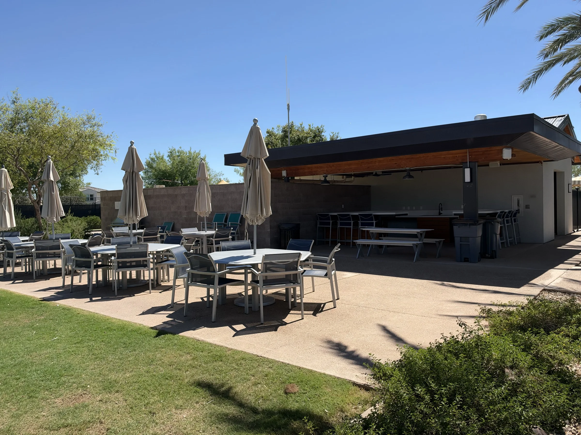 Outdoor tables, umbrellas and a covered gathering area beside the lawn at The Square in Cadence at Gateway.
