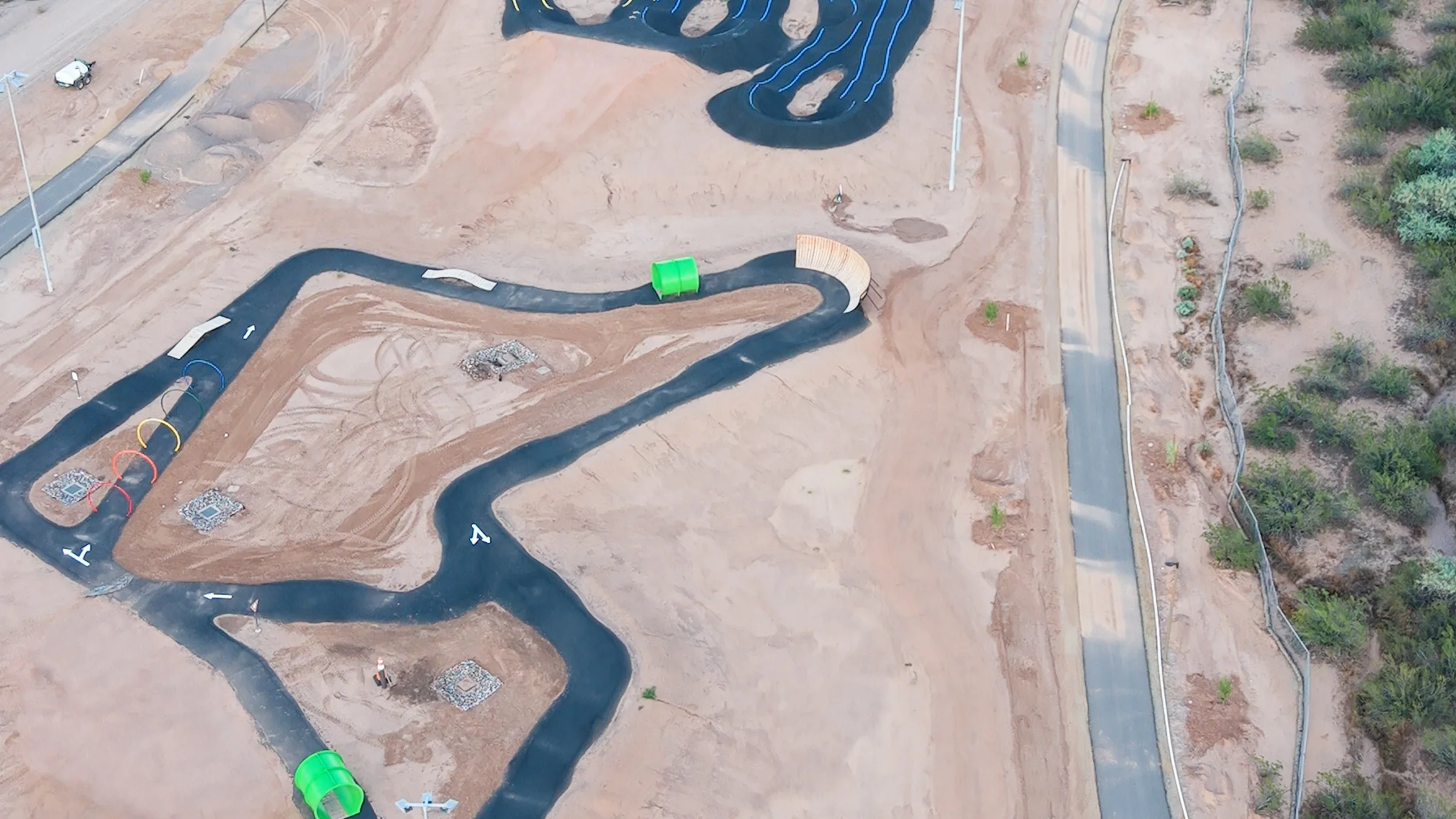 Winding paved bike loop with colored hoops, green tunnels, small ramps and a curved wooden wall at Signal Butte Park.