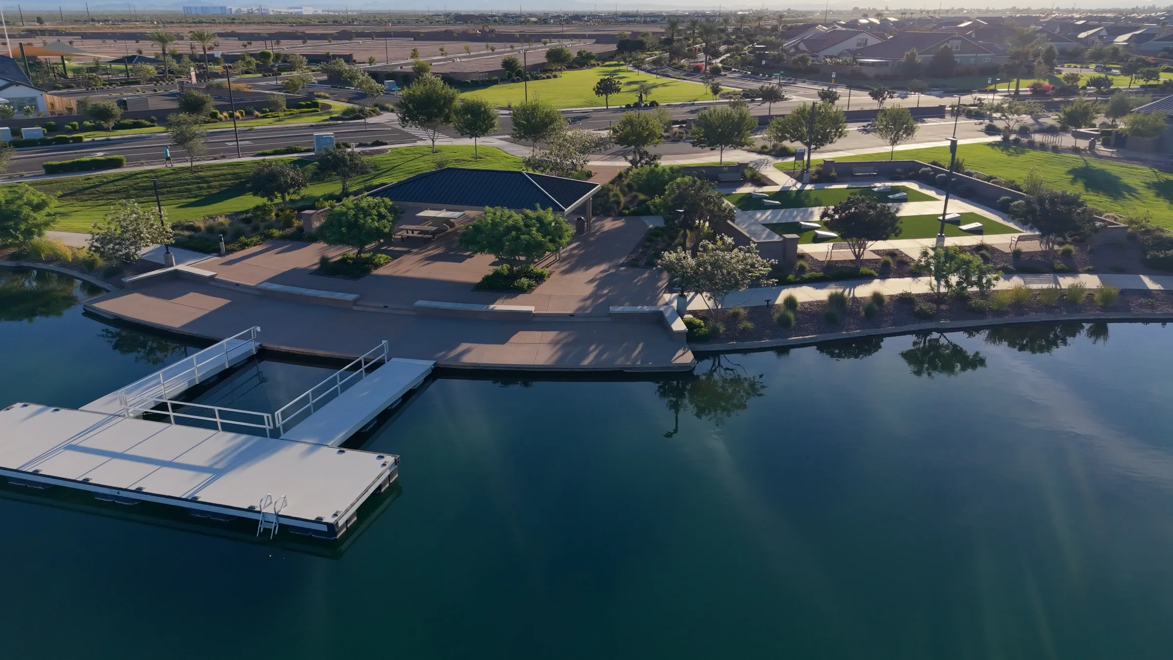 Floating dock beside the Barney Farms lake, with a shaded picnic ramada, cornhole lanes and waterfront landscaping.