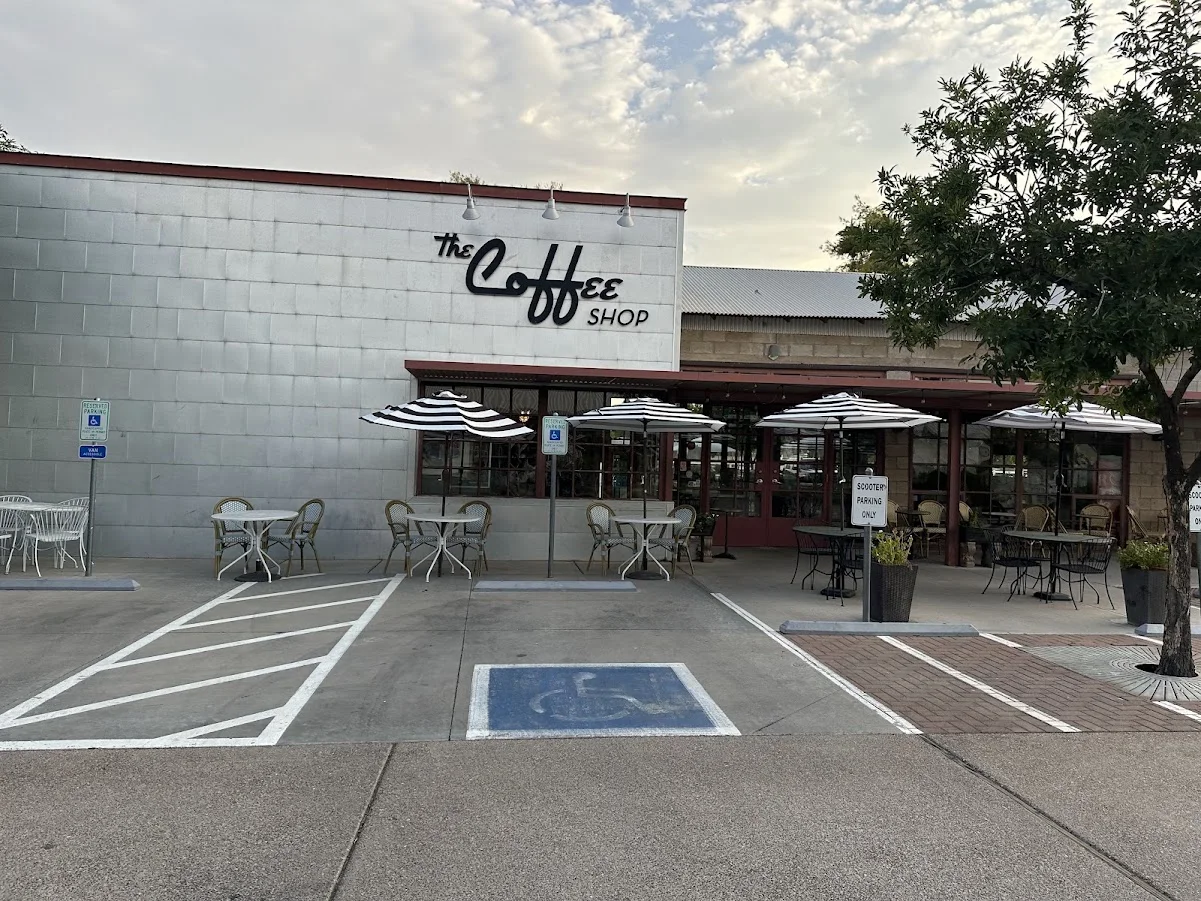 The Coffee Shop at Agritopia with striped patio umbrellas, outdoor tables and marked accessible parking spaces in front.