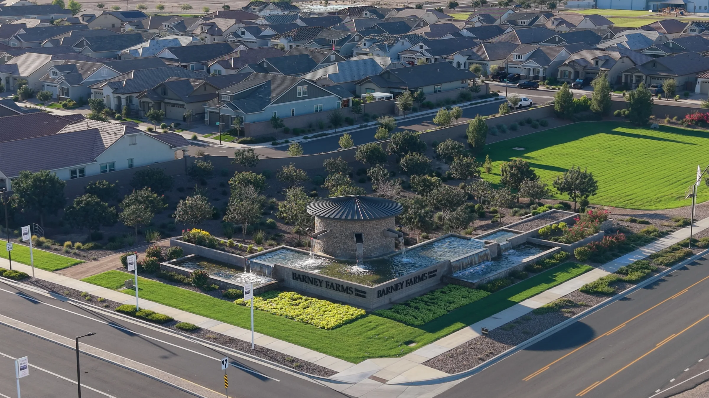 Barney Farms entrance monument with a round stone water feature, cascading fountains, landscaping and neighborhood homes.
