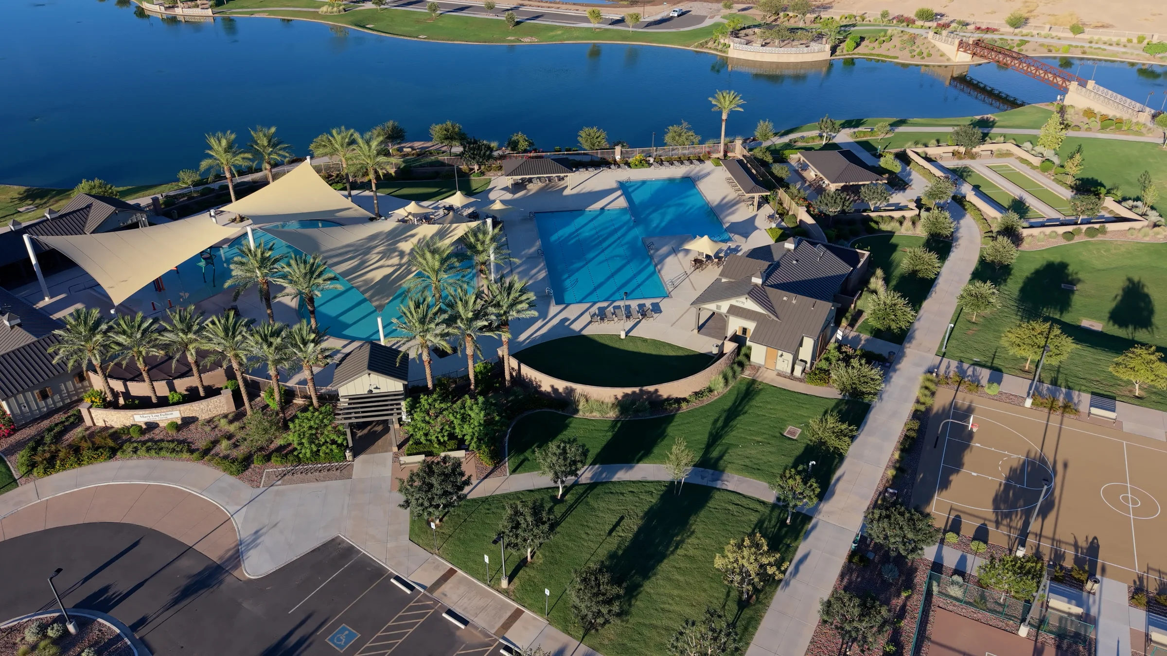 Aerial view of the Barney Farms aquatic center, pools, shade sails and palm trees beside the community lake.