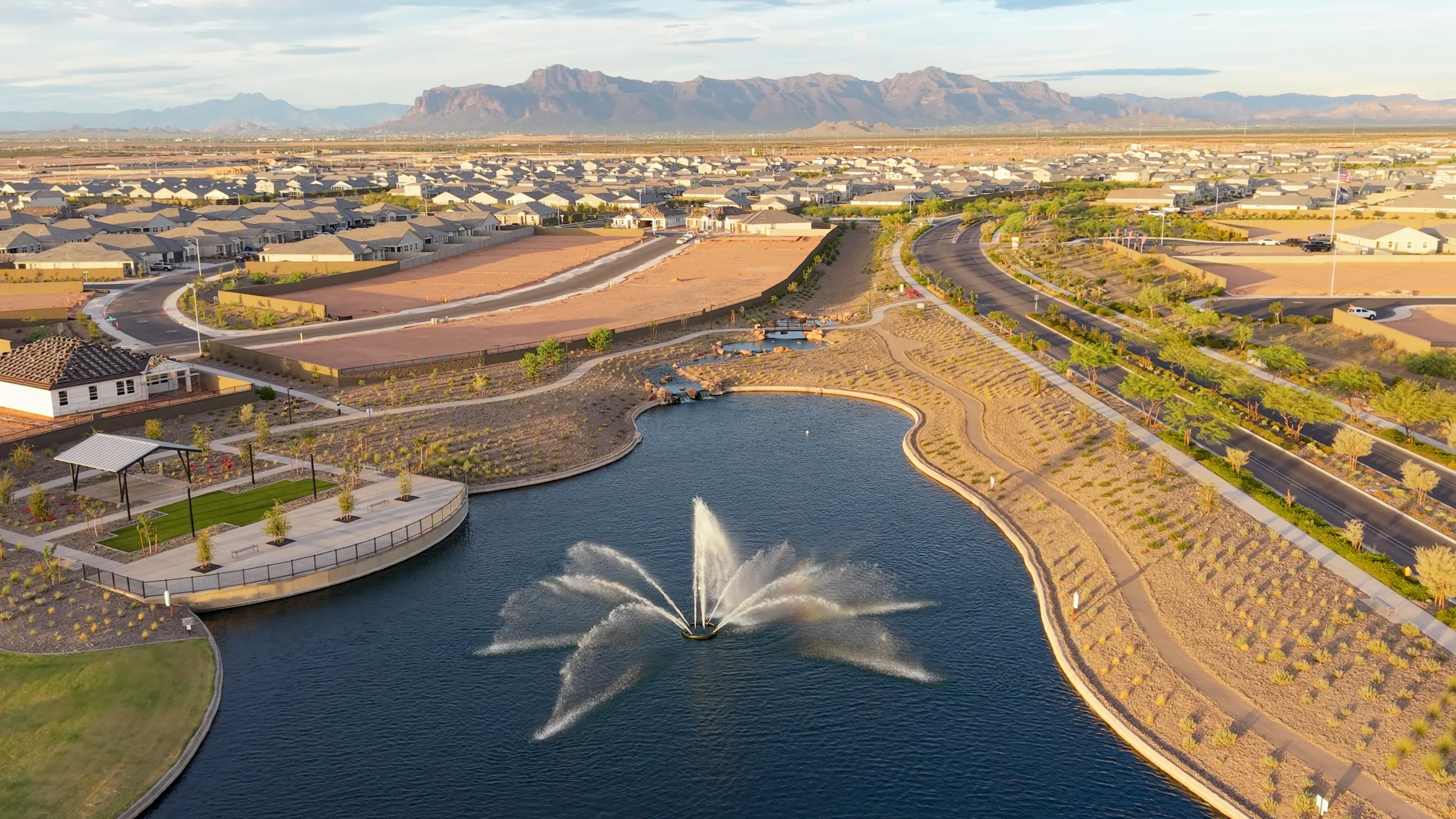 Golden-hour aerial of Radiance’s lake and fountain, with neighborhood homes and the Superstition Mountains beyond.