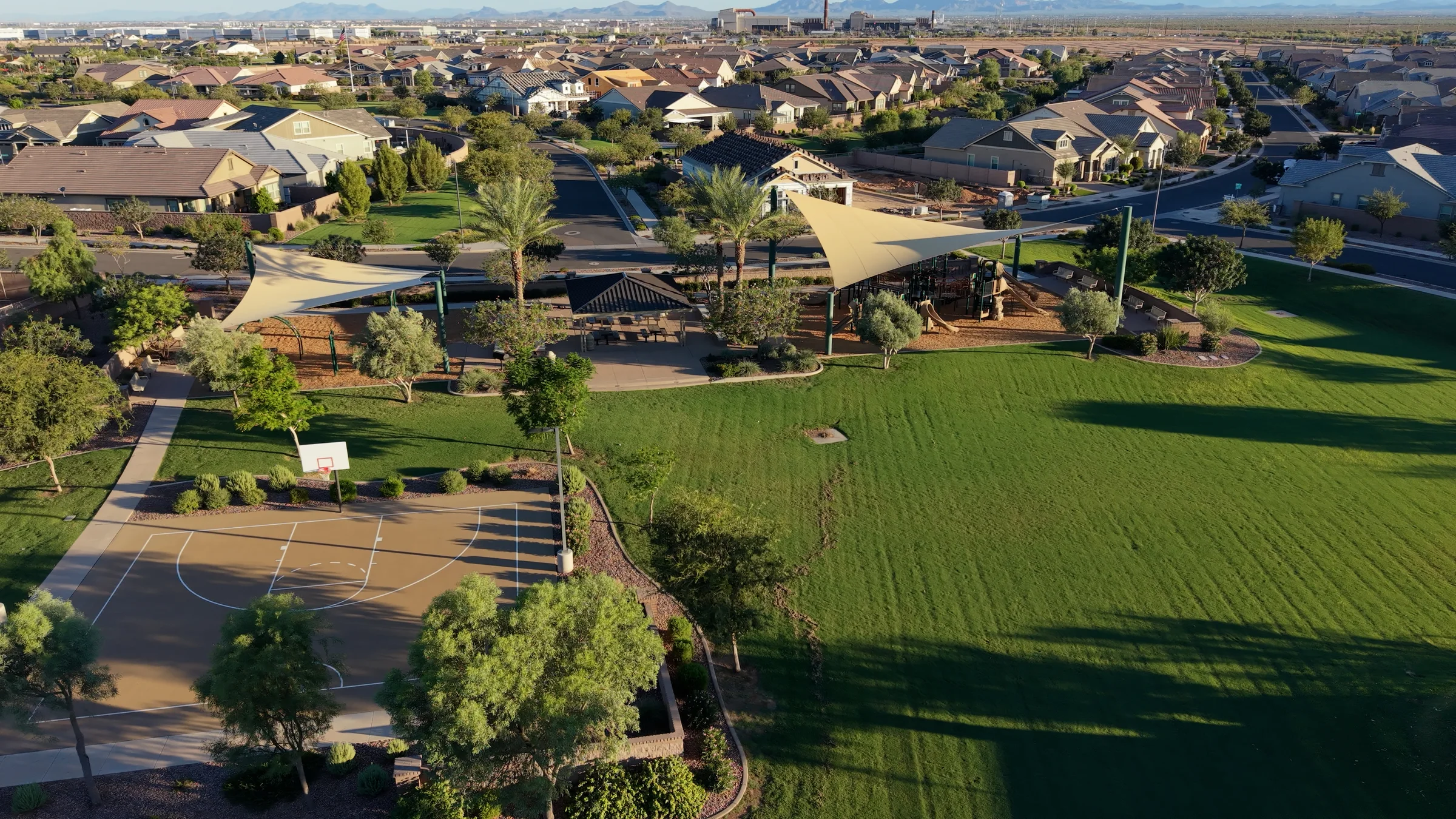 Barney Farms neighborhood park with a basketball court, shaded playgrounds, picnic ramada and green lawn surrounded by homes.