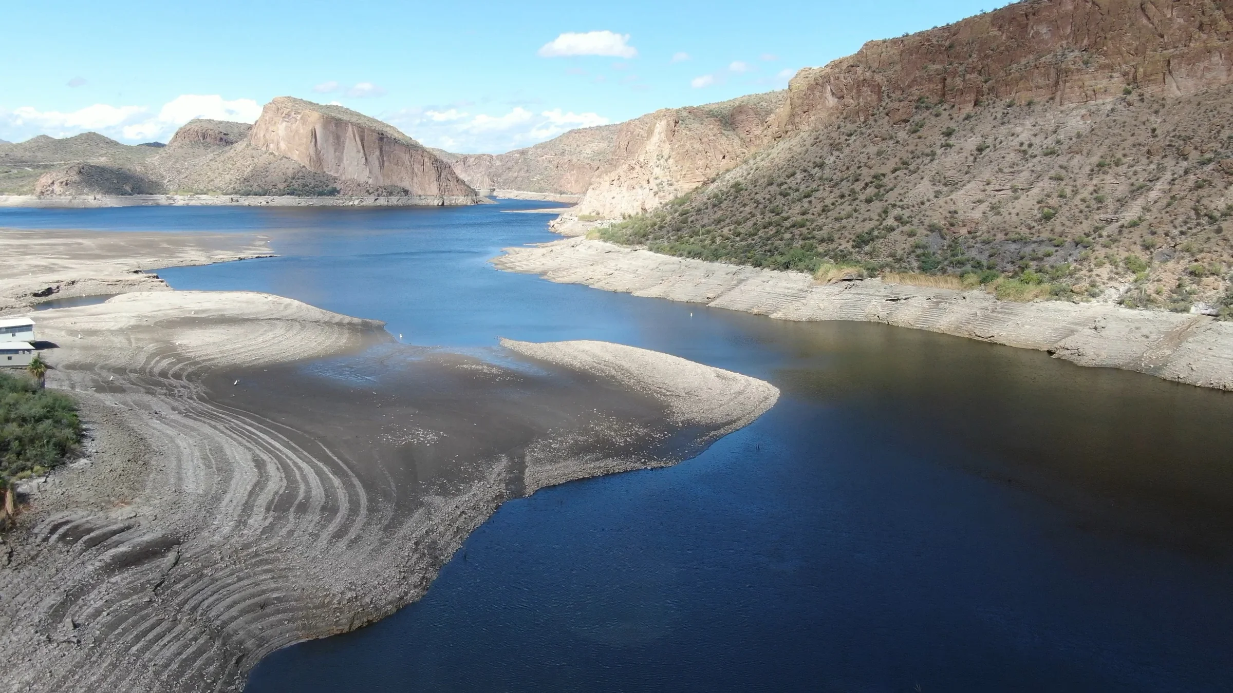 Blue water winds between broad exposed shoreline shelves beneath Canyon Lake's desert cliffs.